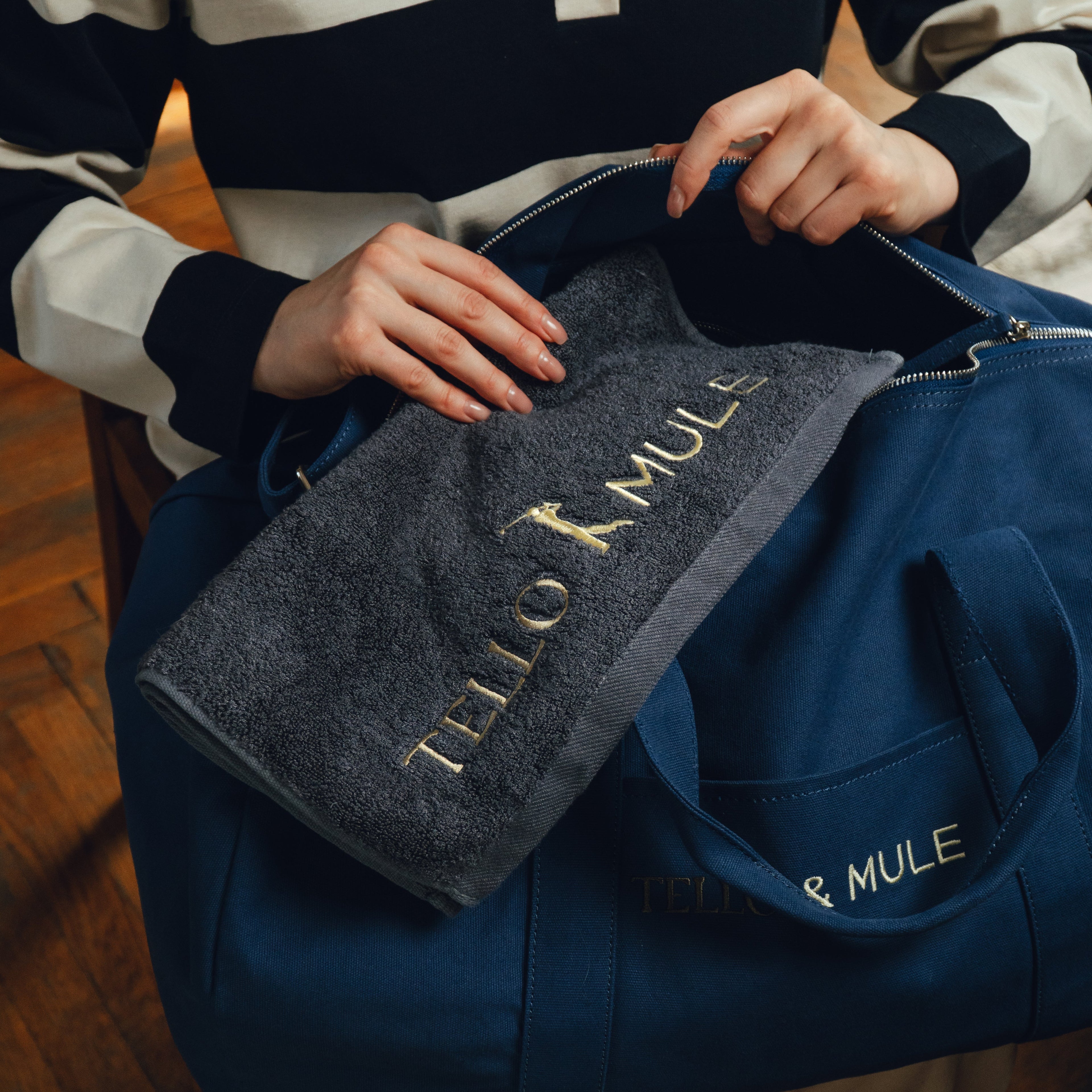 Person holding a blue duffel bag with a towel labeled 'Tello & Mule'.